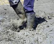 Close-up of wellington boots stamping down wet clay.